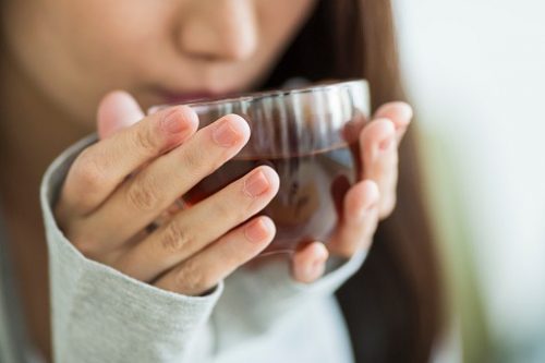 A woman wearing a long-sleeved shirt blows her herbal tea before drinking it. 
